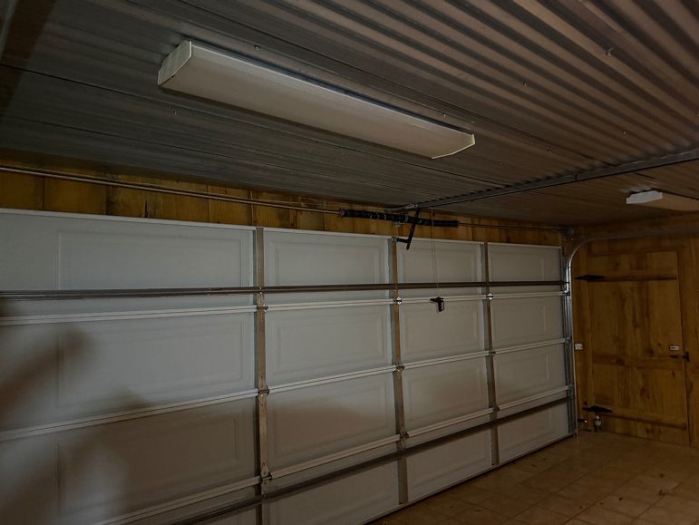 Interior of a garage with a closed white sectional door and overhead light fixtures