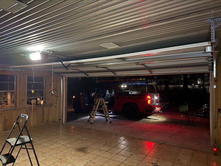 Covered patio/carport at night with a red SUV, ladder, and wet floor reflecting lights.