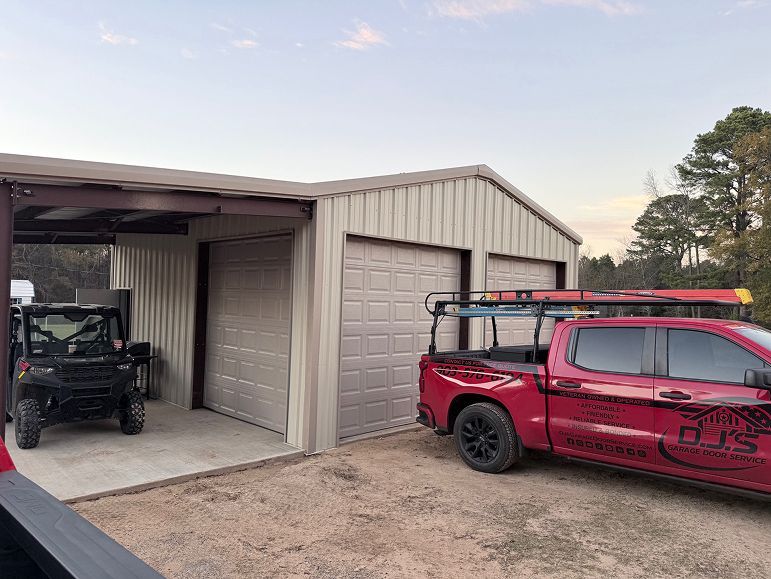 Red off-road truck and ATV parked by a tan garage with open bays.