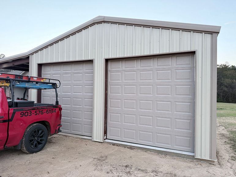 Two beige garage doors on a metal storage building beside a red truck with off-road gear.