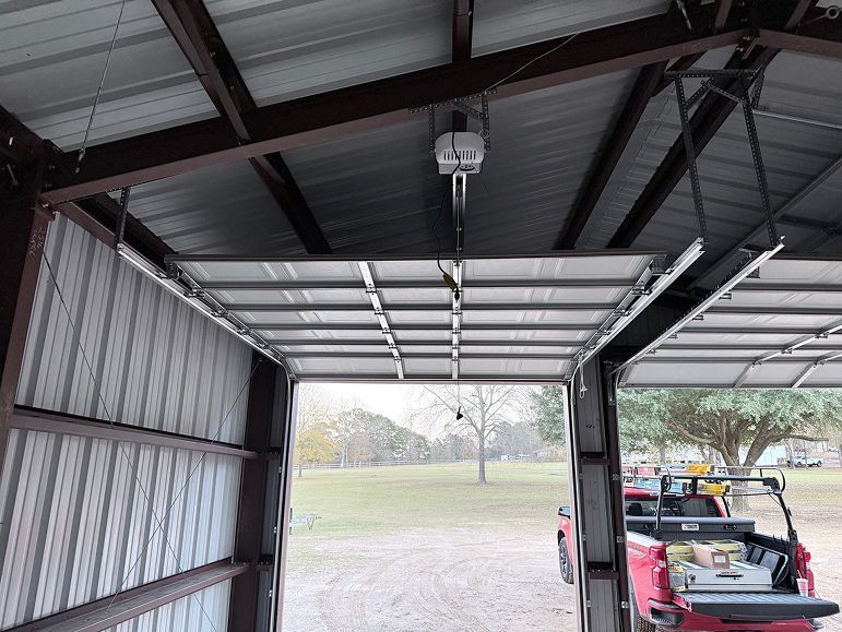 Interior of a metal garage with an open door, showing a parked utility vehicle outside on a gravel driveway.