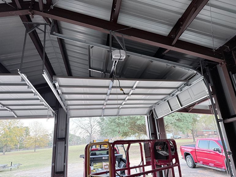 Open garage door with a red pickup truck and a metal frame inside the workshop