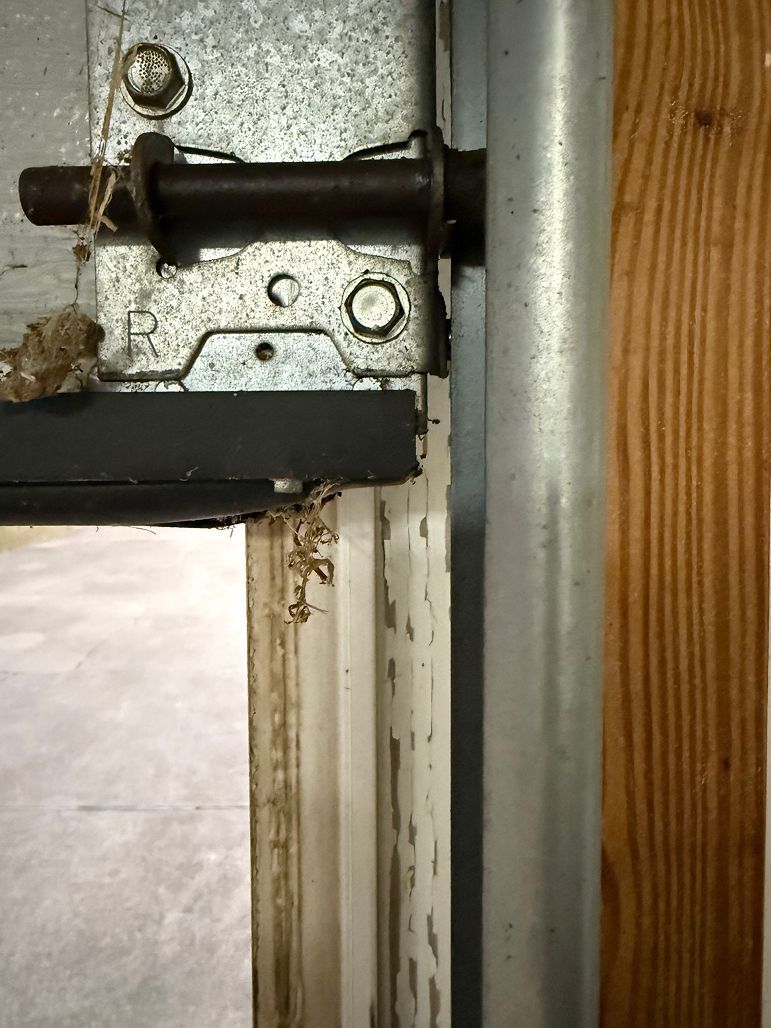 Close-up of a metal door latch and hinge on a white door frame beside wood trim.