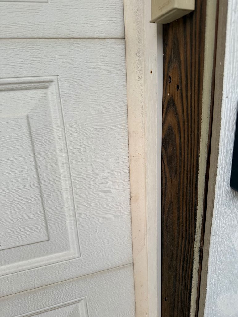 Close-up of a white garage door beside a weathered wooden frame and siding.