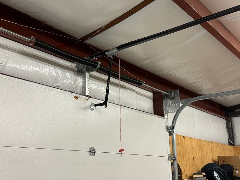 Interior of a garage with exposed ceiling beams, insulation, and a hanging garage door opener cord.