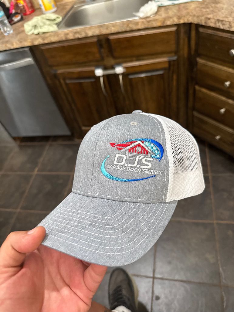 Hand holding a gray mesh baseball cap with a colorful logo in a kitchen.
