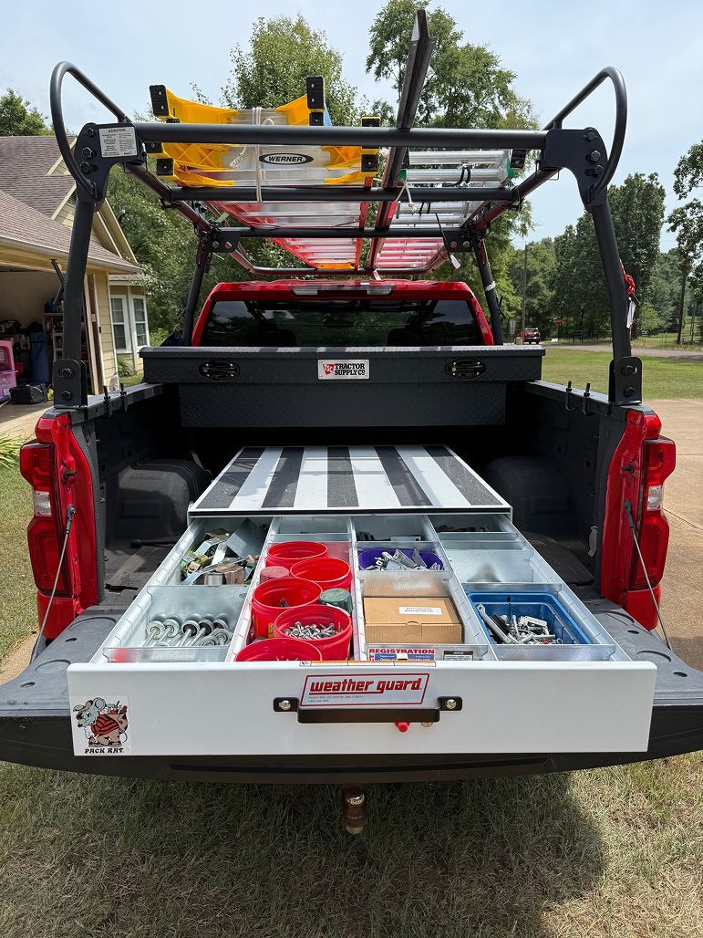 Open utility truck with rear storage drawers and ladder rack, loaded with tools and supplies.