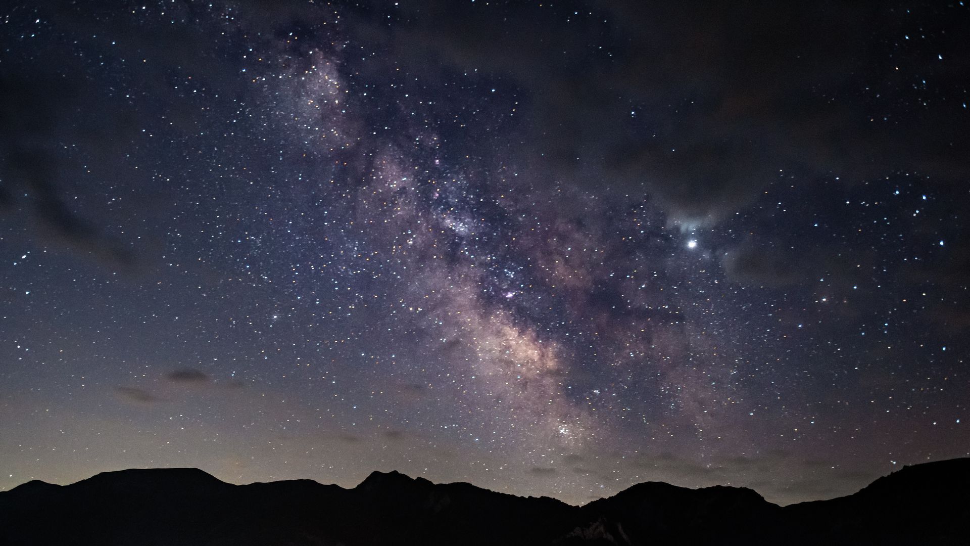 The milky way galaxy is visible in the night sky above the mountains.