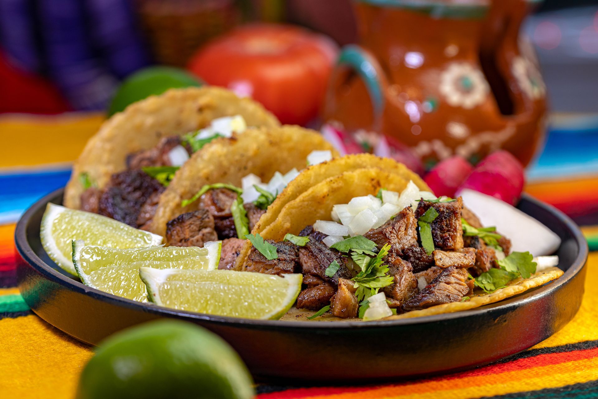 A plate of tacos with limes and sour cream on a table.