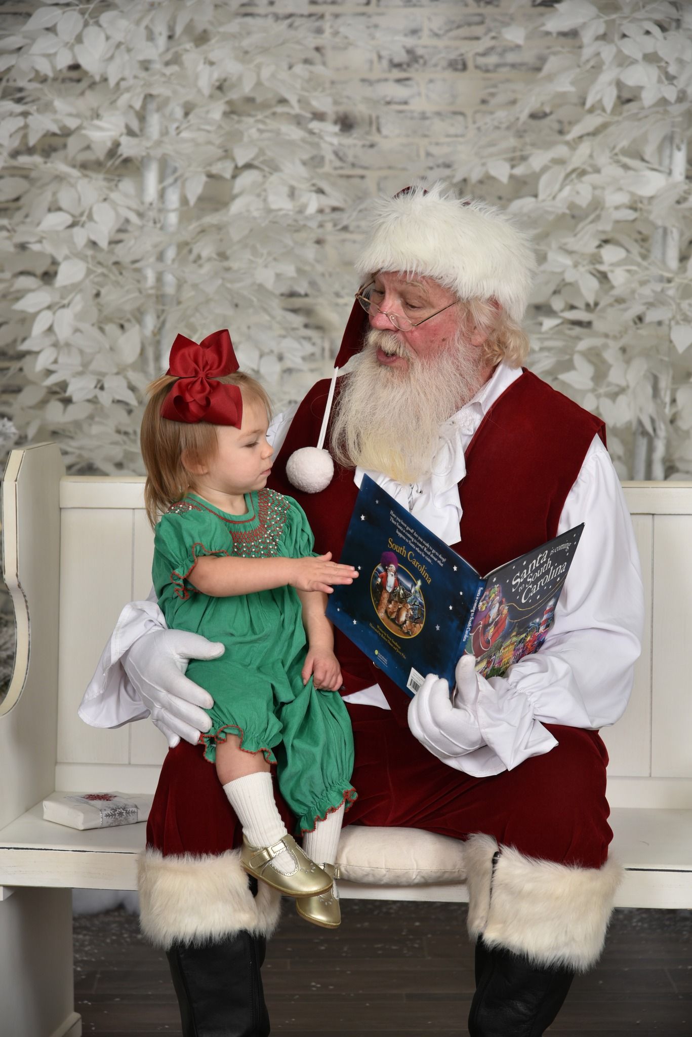 A little girl is sitting on santa 's lap reading a book.