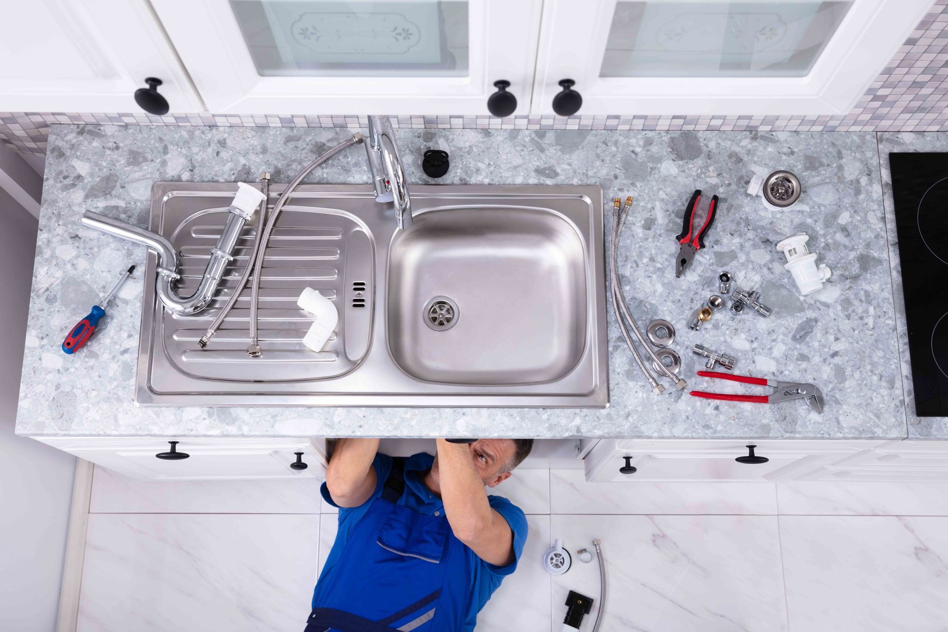 Plumber repairing kitchen sink pipes with tools and fittings. Plumber repairing kitchen sink pipes with tools and fittings.