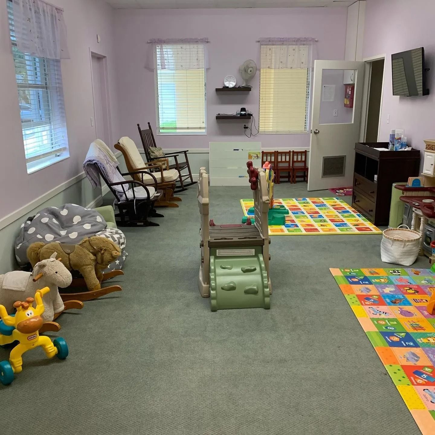 A room with rocking chairs , a rug , and toys.