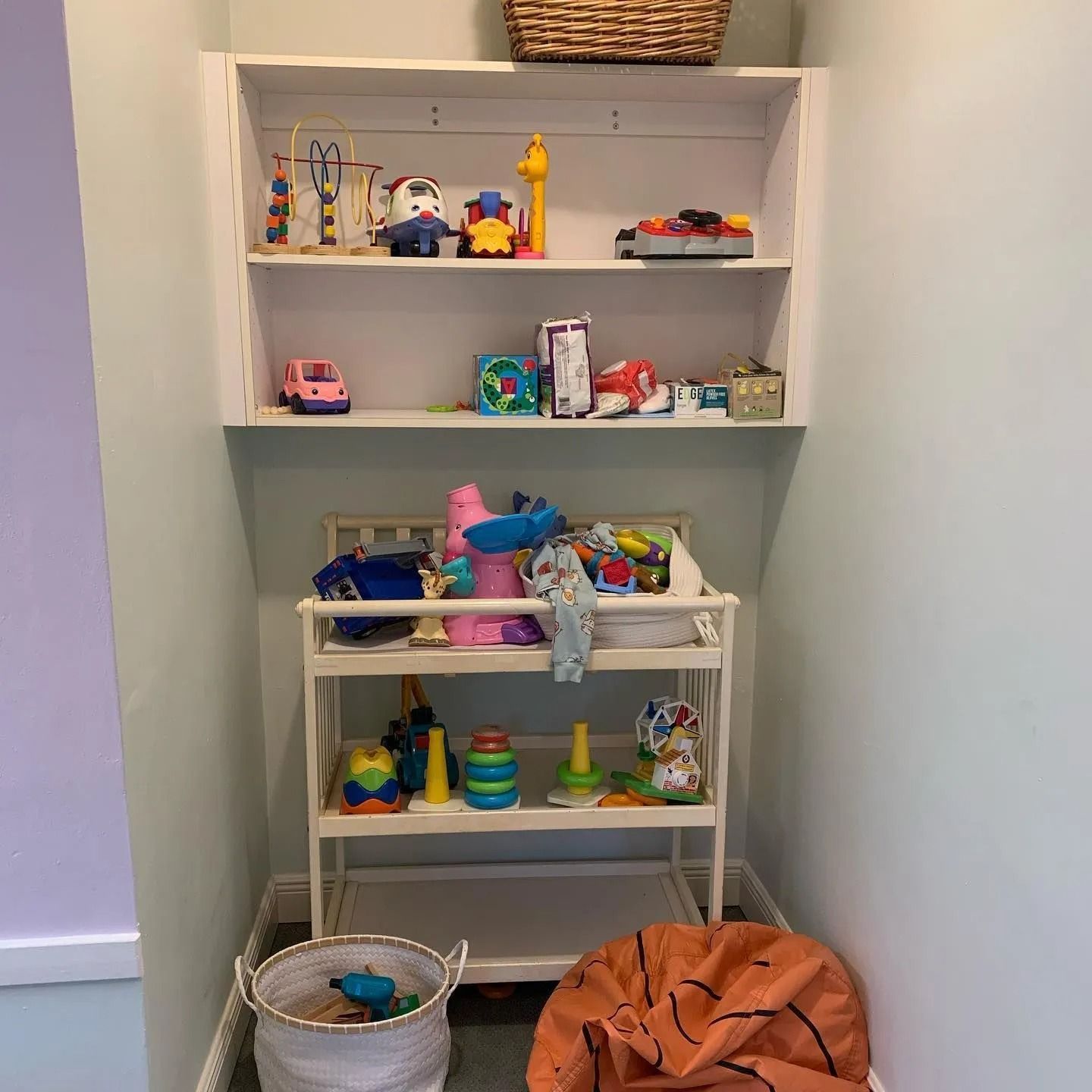 A room with a changing table and shelves filled with toys.