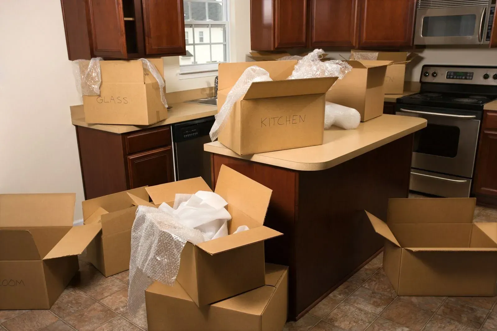 Kitchen with several cardboard moving boxes, some open, on countertops and floor.
