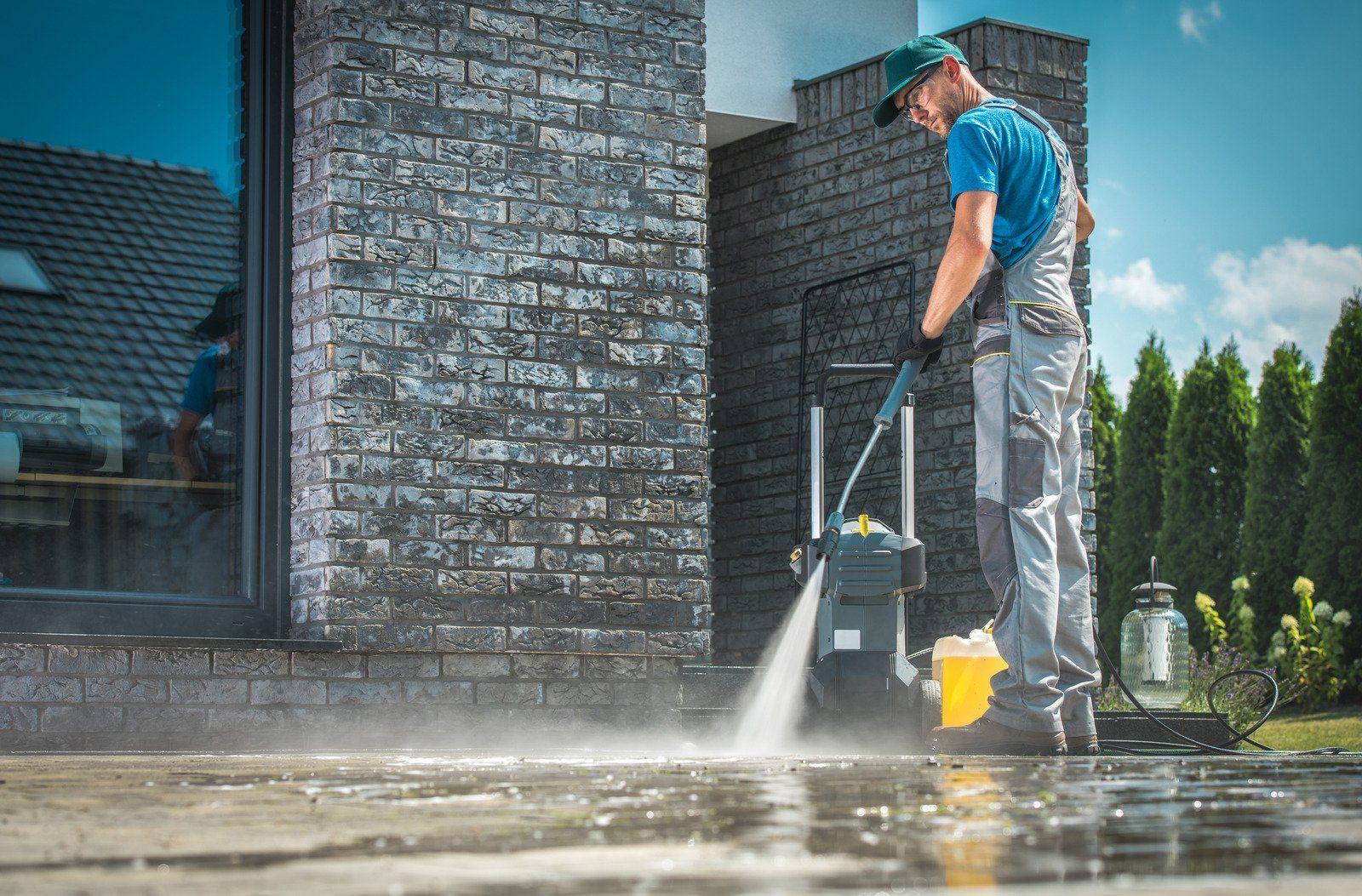 Man power washing a brick patio in front of a house.