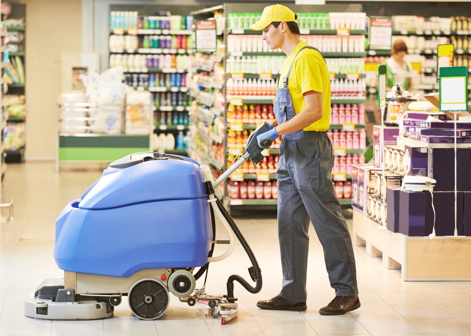 Man using a blue floor cleaning machine in a supermarket aisle.
