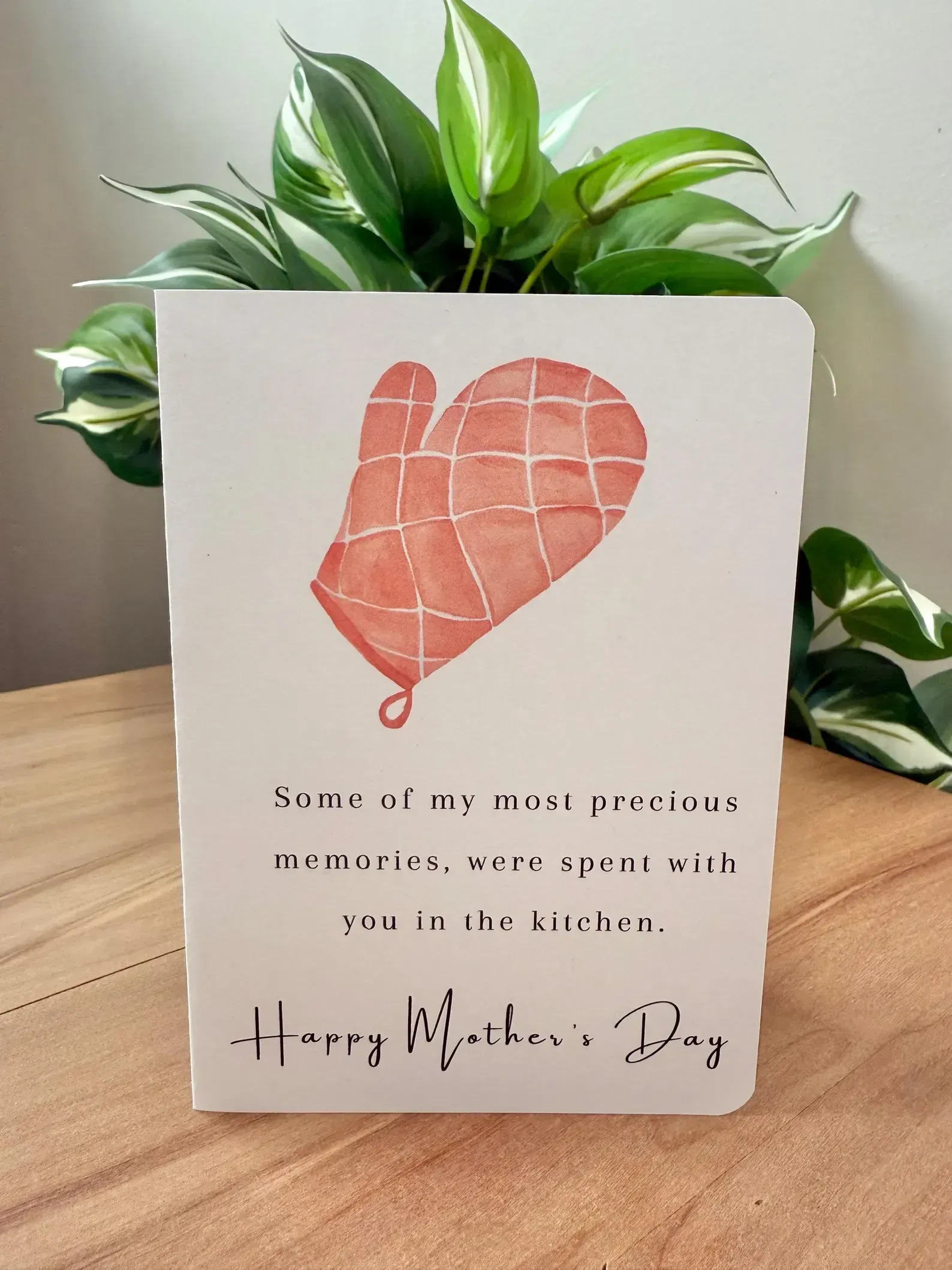 Heart-shaped balloon card on a wooden table with a leafy green plant in the background.