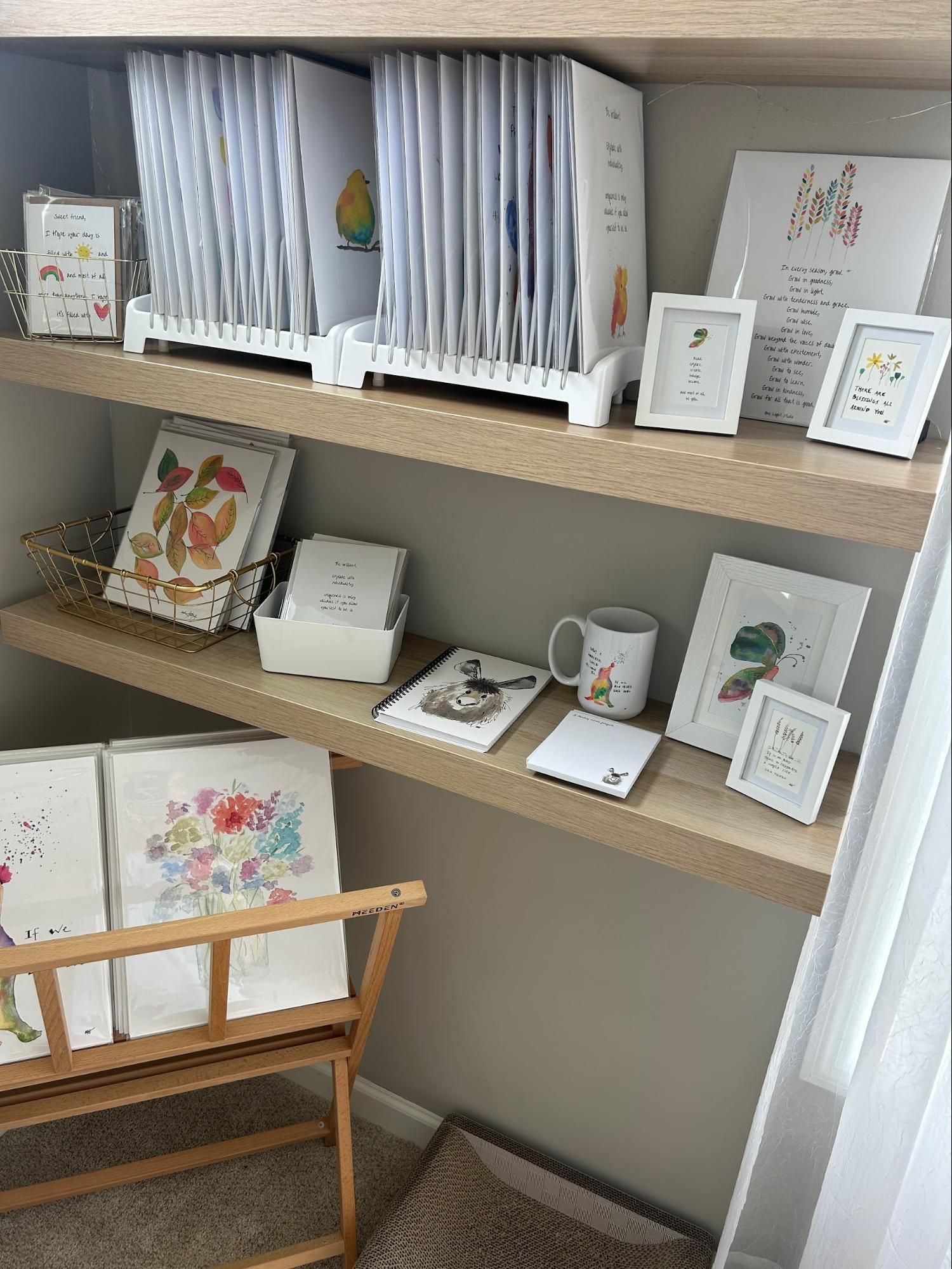 Shelves with books, framed art, and a mug in a well-lit room with a wooden chair.