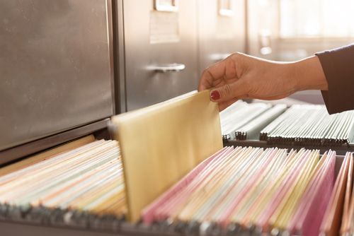 A person is taking a piece of paper out of a filing cabinet.