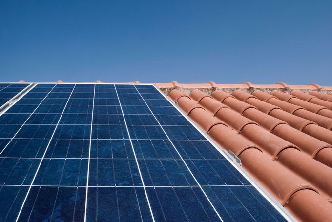 Pannello solare su un tetto di tegole di terracotta contro un cielo azzurro e terso.