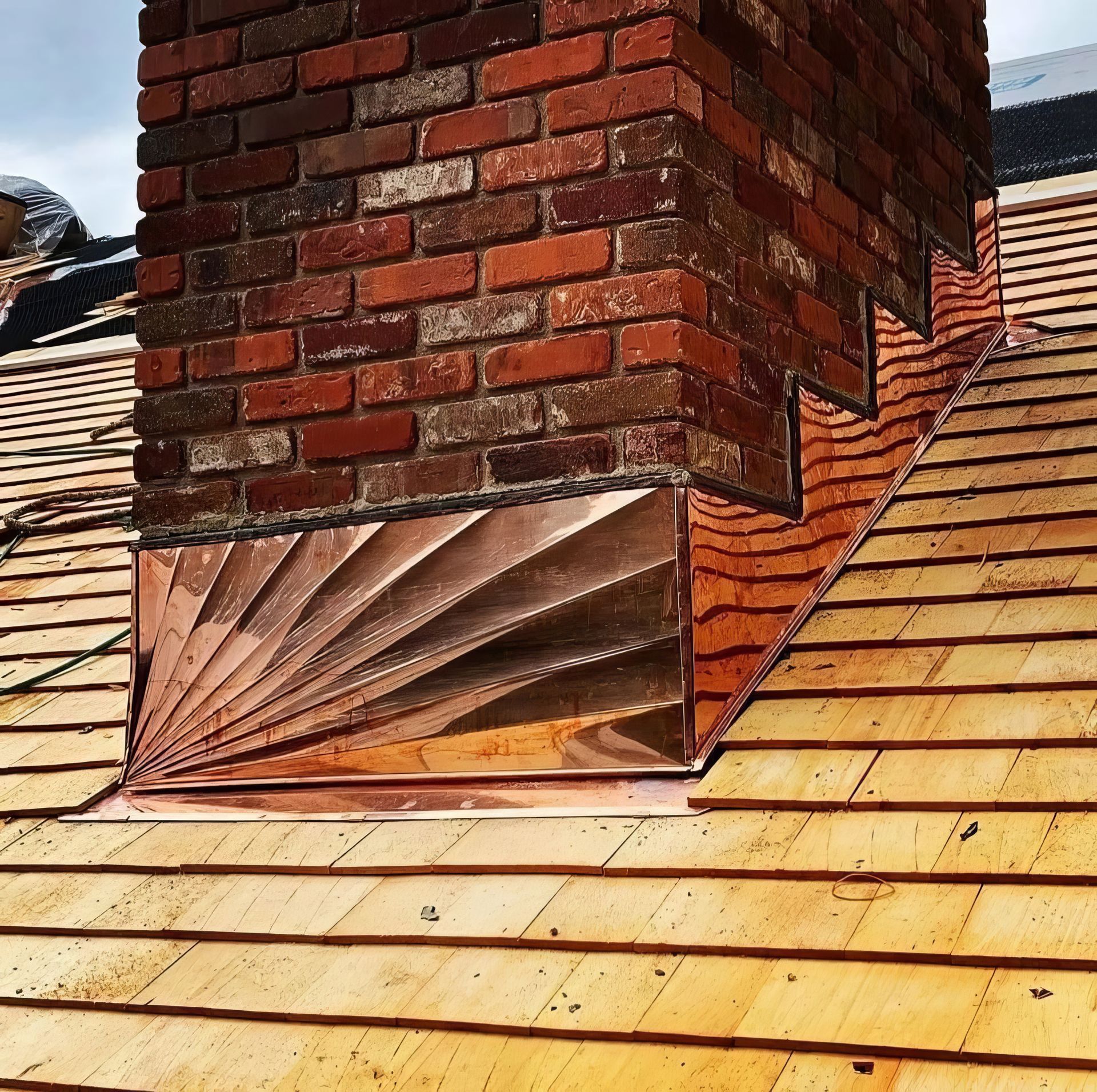 Red metal roof vent flashing around a brick chimney on a shingled roof