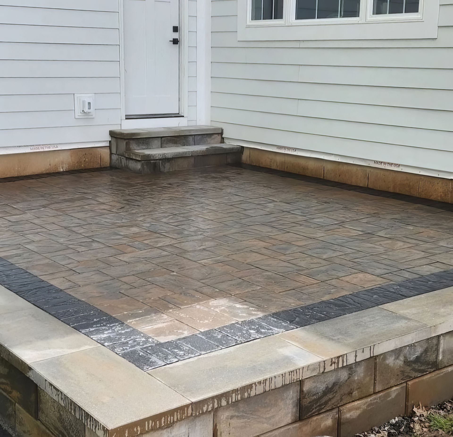 Brick patio with patterned pavers beside a house exterior and back door steps