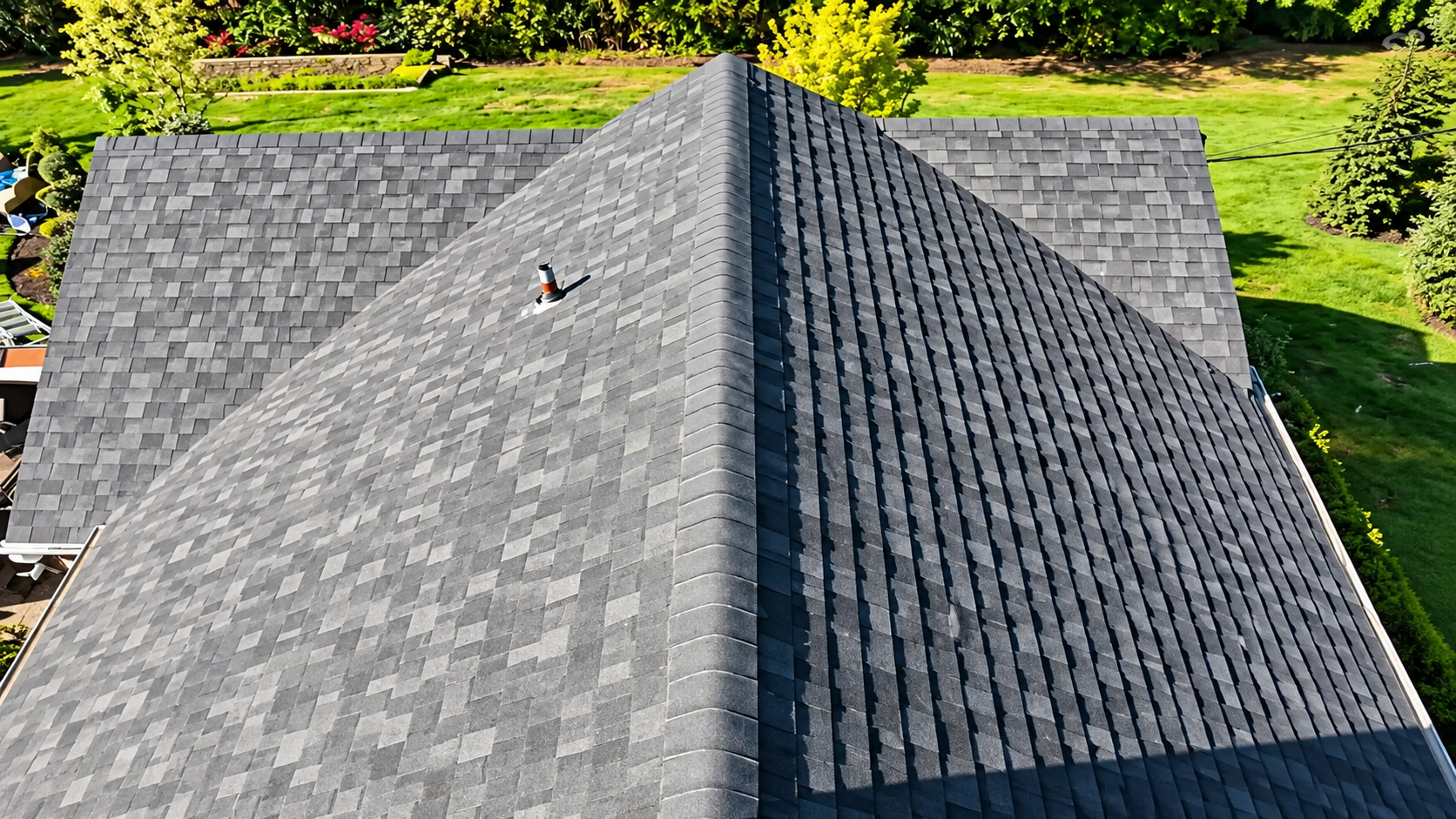 Roof with dark gray shingles and a central ridge, viewed from above against a green yard background