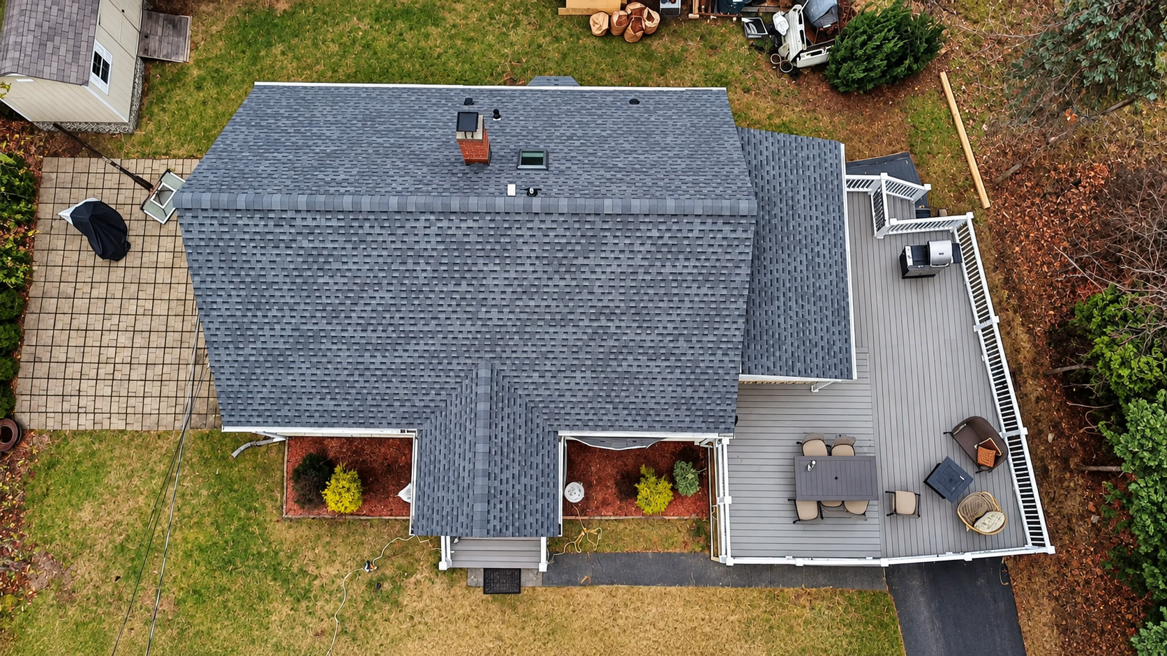 Aerial view of a house with gray shingle roof, brick facade, and a small deck on the right side.