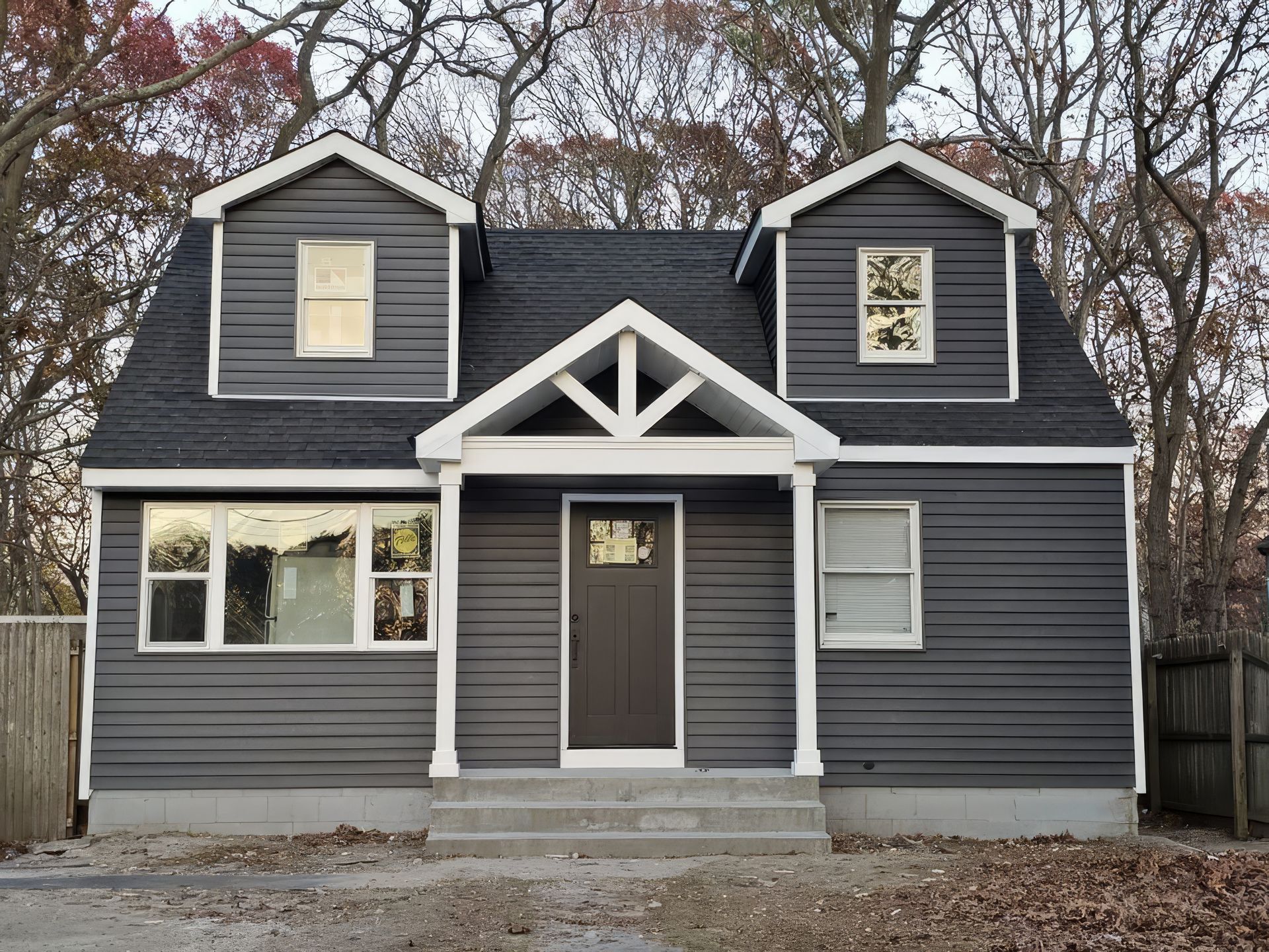 Gray house with white trim and dormer windows, front porch centered among bare trees
