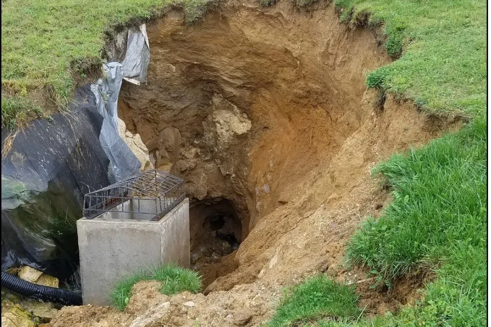 A large sinkhole in the ground with a concrete block in the middle of it.