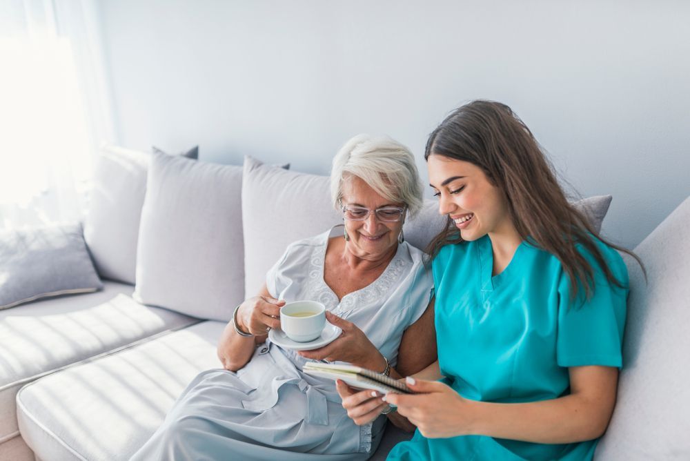 Elderly Woman and Caregiver Seated on Couch, Looking at a Tablet Together — Elder Care at Home in Palm Beach, QLD
