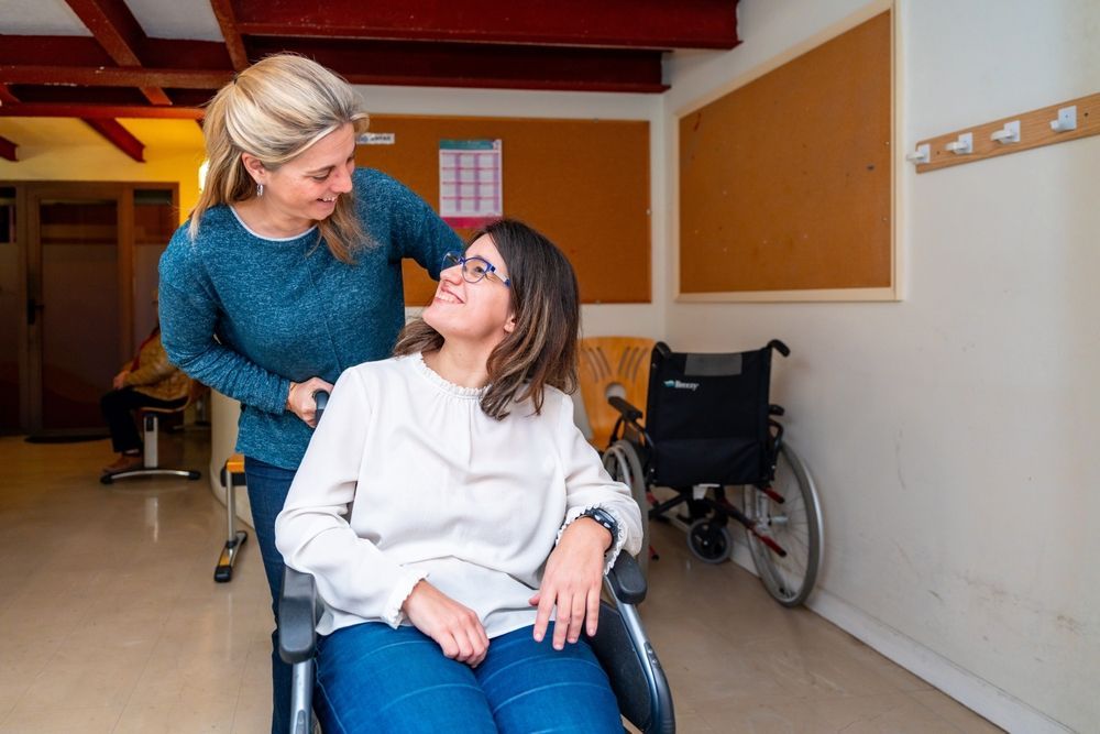 Woman in Wheelchair Smiling at Another Woman Pushing Her, Indoors — Elder Care at Home in Tweed Heads, QLD
