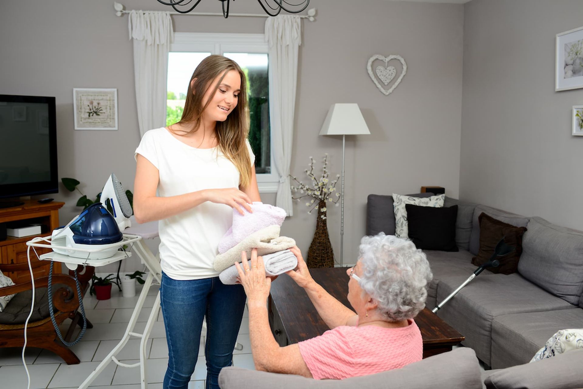 Woman Hands Folded Laundry to An Older Woman in A Living Room — Elder Care at Home in Southport, QLD