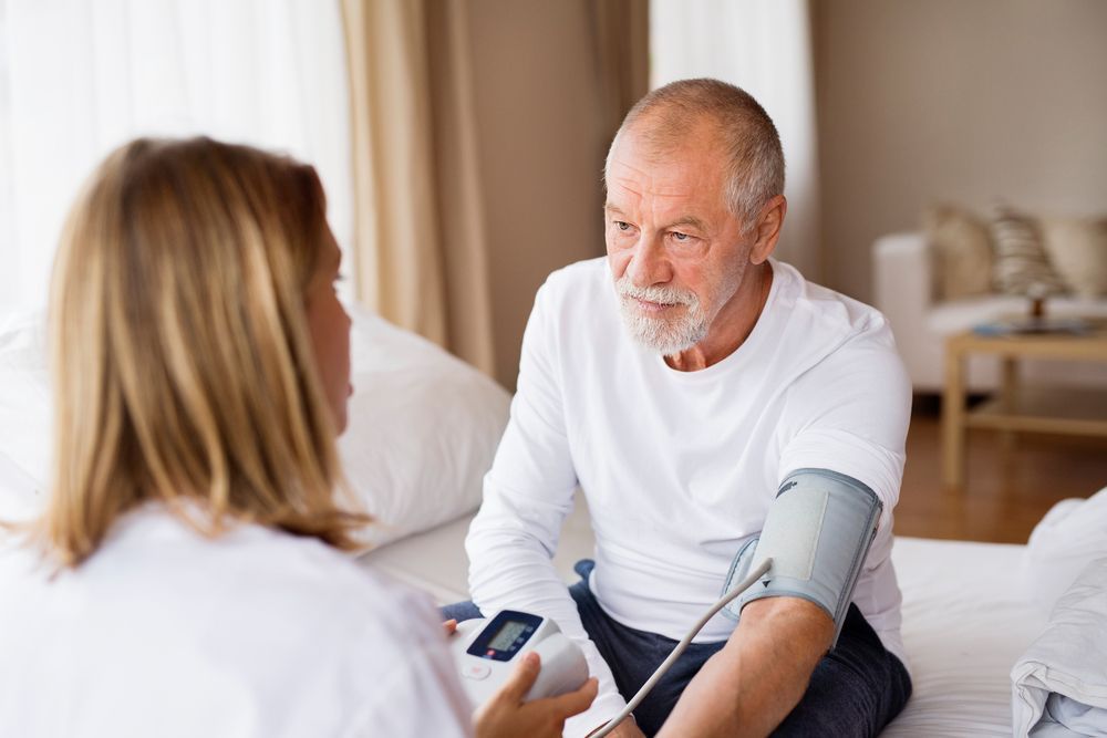 A Healthcare Provider Takes an Older Man's Blood Pressure in a Bedroom — Elder Care at Home in Southport, QLD
