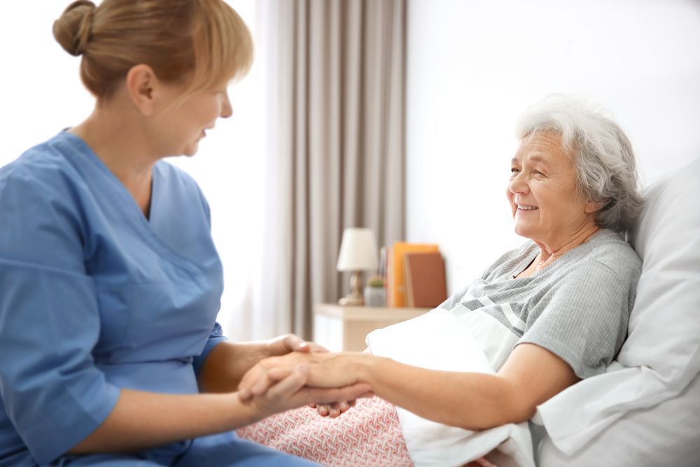 Caregiver in Blue Scrubs Assisting an Elderly Woman at a Kitchen Table — Elder Care at Home in Highland Park, QLD