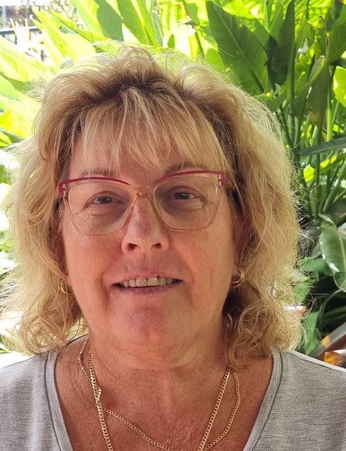 Woman with pink glasses smiling in front of lush green plants — Elder Care at Home in Highland Park, QLD