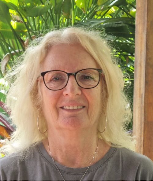 Smiling person with glasses and blonde hair, standing in front of lush green plants. — Elder Care at Home in Highland Park, QLD