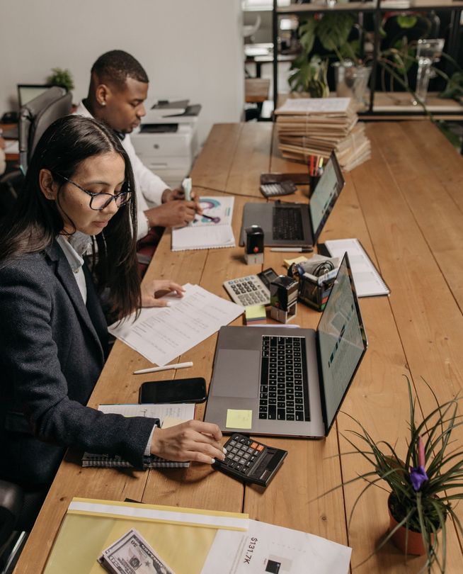 A woman is sitting at a desk with a laptop and a calculator.