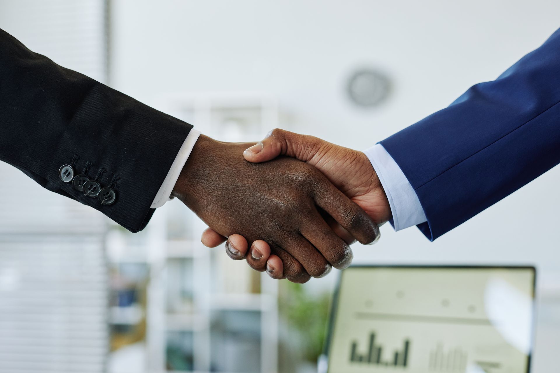 Two men in suits are shaking hands in an office.