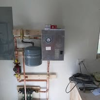 A boiler system with copper pipes, a gray tank, and a control panel mounted on a wall.