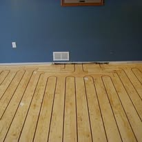 Light wood floor with dark lines forming a radiant heating system pattern in front of a blue wall.