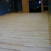 Light wood flooring installed on a foundation, blue wall in background.