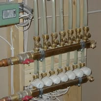 Piping system with brass manifolds, clear tubes, and white control knobs, mounted on wood.