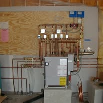 Copper piping and HVAC equipment mounted on plywood wall.