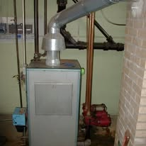 A furnace with pipes and a chimney in a basement setting.