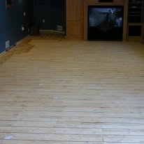 Light-colored wooden floor in a room, with a dark blue wall on the left side and a fireplace.