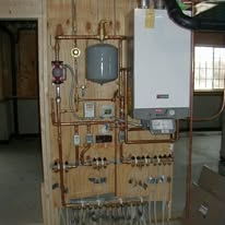 Copper pipe and heating equipment mounted on a wooden panel, including a water heater and expansion tank.