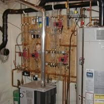 Copper pipes, pumps, and a water heater mounted on a wooden panel in a basement.