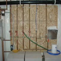 Copper plumbing pipes and valves mounted on an OSB board in a basement.