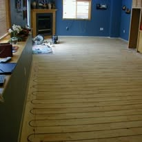Wooden floor with grooves for underfloor heating in a room with a fireplace.